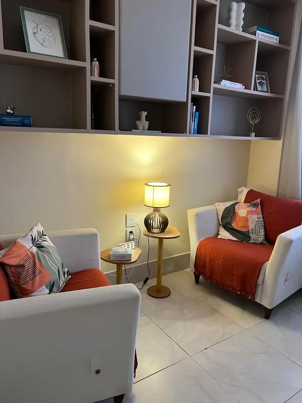 Consultório com sofá, poltronas em tom terracota, estante e iluminação acolhedora